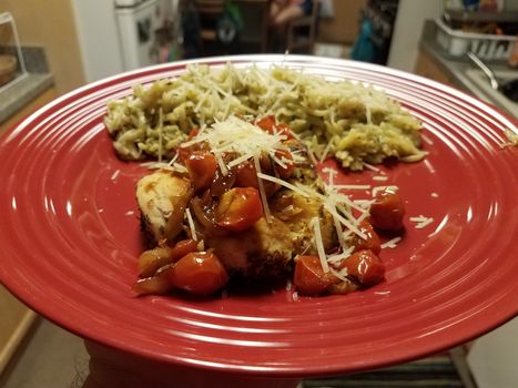 red plate with chicken and tomato and orzo pasta in kitchen