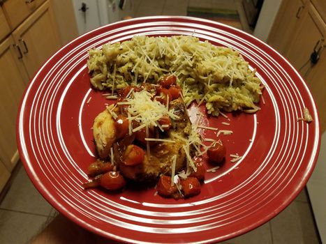 red plate with chicken and tomato and orzo pasta in kitchen