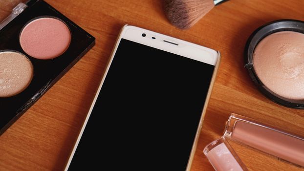 Smartphone with empty screen and cosmetics on light wooden background. Top view, flat lay. Mobile phone mockup.