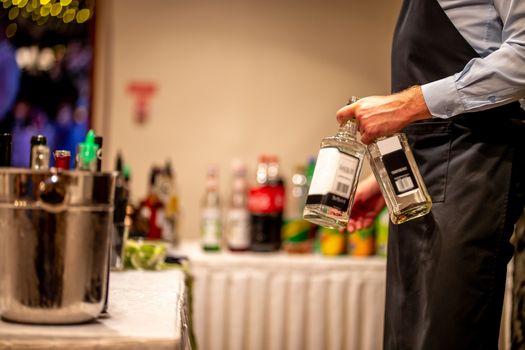 Waiter holds two whiskey bottles in hand. Waiter with two whiskey bottles in wedding party. Ice bucket with wine bottles.