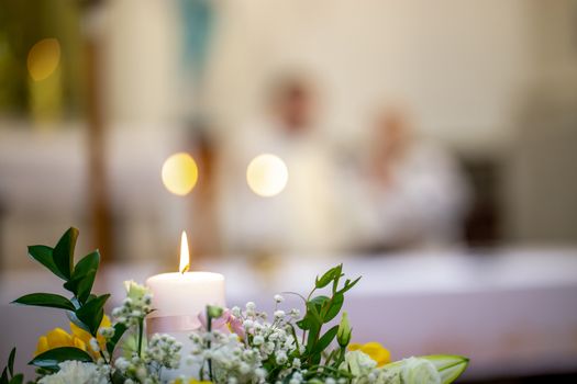 Fragment of burning candle and bouquet of flowers during wedding in church, Latvia. Closeup of wedding flowers bouquet and burning candle on blurred background..