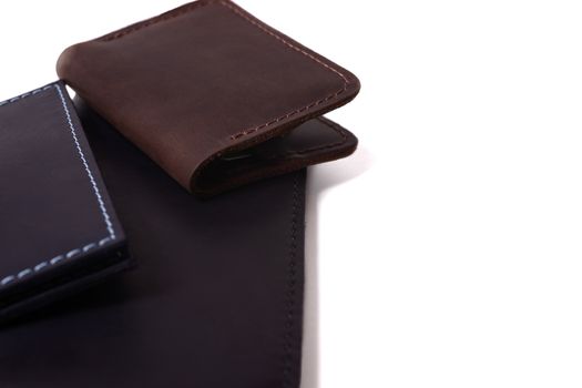 Handmade leather brown cardholder, blue passport cover and black purse isolated on white background closeup. Stock photo of isolated handmade luxury accessories.