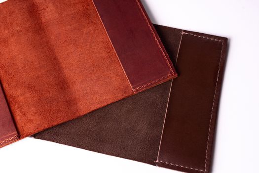Two handmade leather passport covers isolated on white background. Closeup view. Covers are red, brown and open.