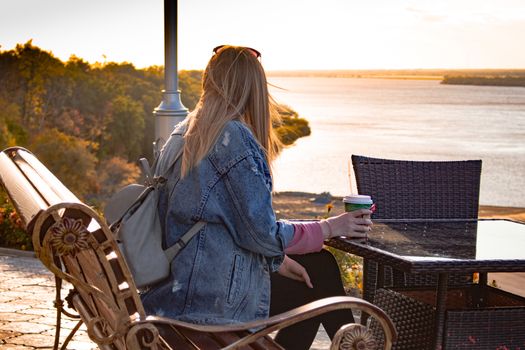 Girl drinking coffee and watching the sunset from the river