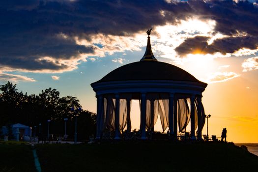 A couple in love hugs and kisses next to a romantic gazebo against the sunset