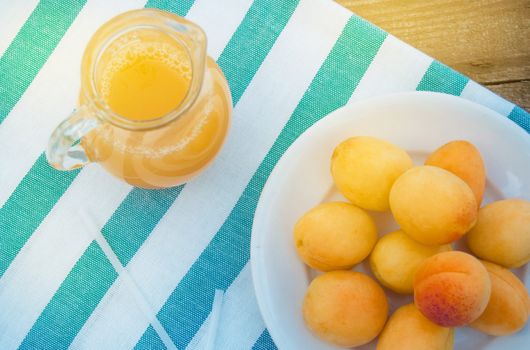 Summer drink and fruit-fresh apricot juice in a glass jug and ripe apricots on a napkin, top view, outdoor.