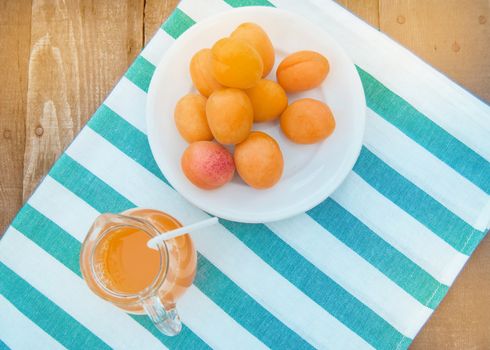 Summer drink and fruit-fresh apricot juice in a glass jug and ripe apricots on a napkin, top view, outdoor.