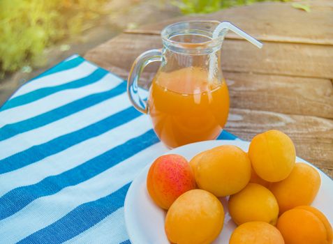 Summer drink and fruit-fresh apricot juice in a glass jug and ripe apricots on a napkin, outdoors on a Sunny day.