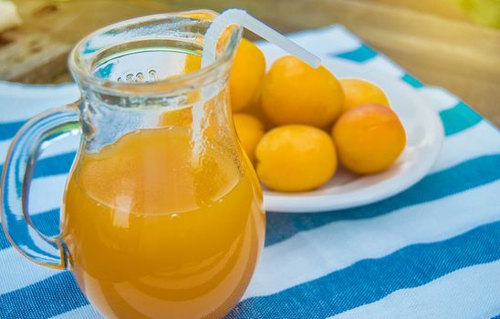 Summer drink and fruit-fresh apricot juice in a glass jug and ripe apricots on a napkin, outdoors on a Sunny day.