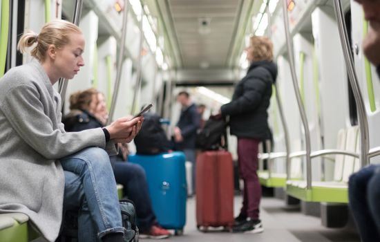 Beautiful blonde caucasian woman wearing winter coat reading on the phone while traveling by metro. Public transportation concept.