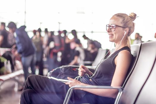 Casual sporty young blond female traveler using her cell phone while waiting to board a plane at the departure gates at the asian airport terminal.