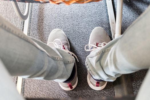 Male passenger with lack of leg space on long commercial airplane flight. Focus on casual sporty sneakers.