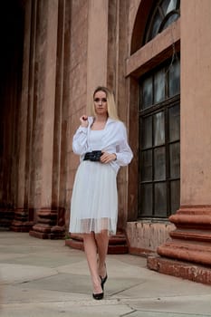 Fashion look's woman. Young woman modern portrait. Young woman dressed in white skirt and shirt posing near the old looking soviet union's architectural building with large pillars and bas-reliefs.