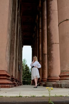 Fashion look's woman. Young woman modern portrait. Young woman dressed in white skirt and shirt posing near the old looking soviet union's architectural building with large pillars and bas-reliefs.