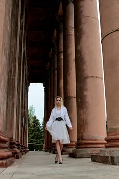 Fashion look's woman. Young woman modern portrait. Young woman dressed in white skirt and shirt posing near the old looking soviet union's architectural building with large pillars and bas-reliefs.