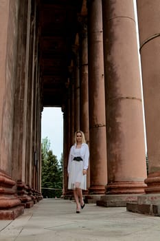 Fashion look's woman. Young woman modern portrait. Young woman dressed in white skirt and shirt posing near the old looking soviet union's architectural building with large pillars and bas-reliefs.