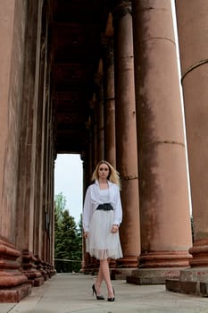 Fashion look's woman. Young woman modern portrait. Young woman dressed in white skirt and shirt posing near the old looking soviet union's architectural building with large pillars and bas-reliefs.