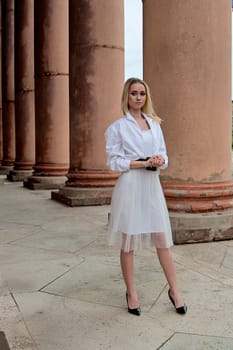 Fashion look's woman. Young woman modern portrait. Young woman dressed in white skirt and shirt posing near the old looking soviet union's architectural building with large pillars and bas-reliefs.