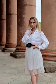 Fashion look's woman. Young woman modern portrait. Young woman dressed in white skirt and shirt posing near the old looking soviet union's architectural building with large pillars and bas-reliefs.