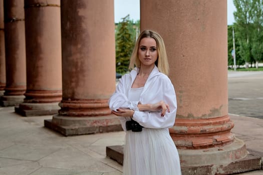 Fashion look's woman. Young woman modern portrait. Young woman dressed in white skirt and shirt posing near the old looking soviet union's architectural building with large pillars and bas-reliefs.