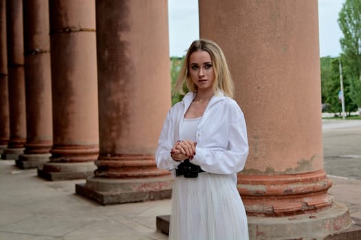 Fashion look's woman. Young woman modern portrait. Young woman dressed in white skirt and shirt posing near the old looking soviet union's architectural building with large pillars and bas-reliefs.