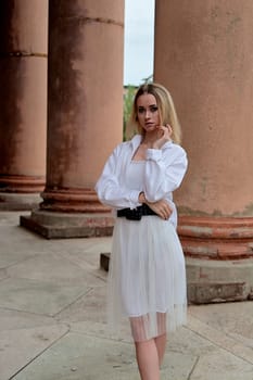 Fashion look's woman. Young woman modern portrait. Young woman dressed in white skirt and shirt posing near the old looking soviet union's architectural building with large pillars and bas-reliefs.