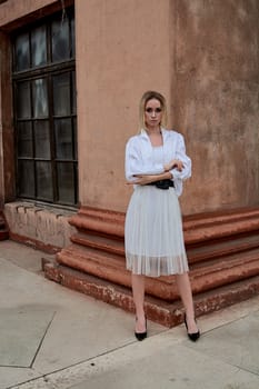 Fashion look's woman. Young woman modern portrait. Young woman dressed in white skirt and shirt posing near the old looking soviet union's architectural building with large pillars and bas-reliefs.