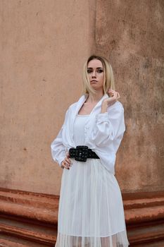 Fashion look's woman. Young woman modern portrait. Young woman dressed in white skirt and shirt posing near the old looking soviet union's architectural building with large pillars and bas-reliefs.