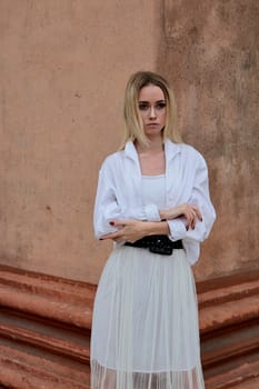 Fashion look's woman. Young woman modern portrait. Young woman dressed in white skirt and shirt posing near the old looking soviet union's architectural building with large pillars and bas-reliefs.