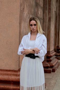 Fashion look's woman. Young woman modern portrait. Young woman dressed in white skirt and shirt posing near the old looking soviet union's architectural building with large pillars and bas-reliefs.