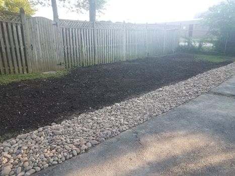 asphalt driveway with stones or rocks and dirt and wood fence