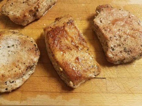 cooked pork chops with seasoning on wood cutting board and juices