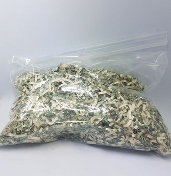 plastic bag of shredded united states dollar bills on white background