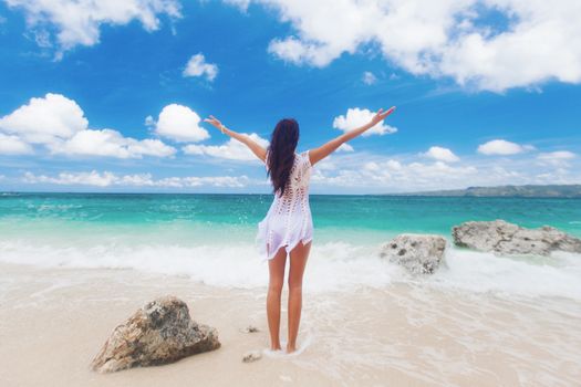 Summer freedom on the beach. Joyful woman raising arms to the sky, enjoying travel and vacation on tropical beach