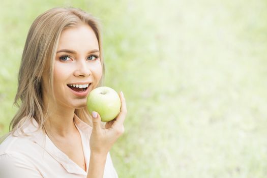 Young woman holding fresh green apple on spring grass background