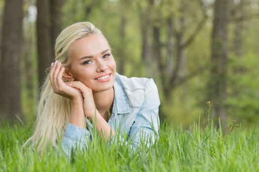 Blonde pretty girl laying on the grass in spring park and smiling