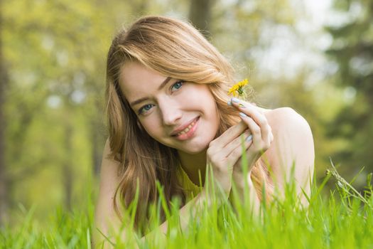 Blonde pretty girl laying on the grass in spring park and smiling