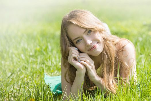 Blonde pretty girl laying on the grass in spring park and smiling