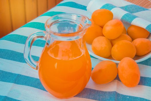 Summer drink - fresh apricot juice in a glass jug, next to the apricots are on a striped napkin.