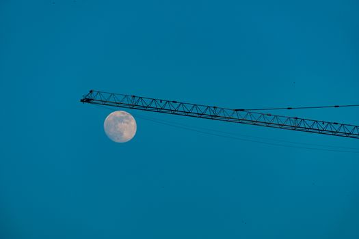 Crane on a construction site against blue sky and a moon