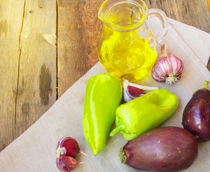 Raw eggplant, garlic, olive oil, sweet pepper, healthy eating and diet concept on an old wooden background with copy space.