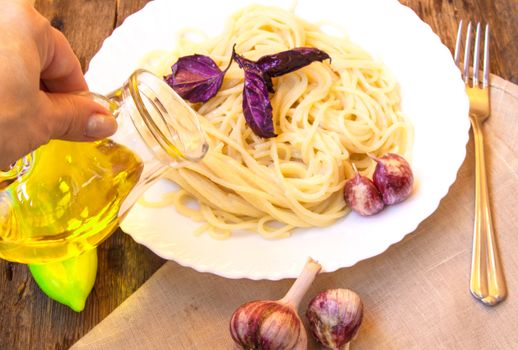 Italian cuisine, spaghetti with Basil and garlic, a woman's hand holding a glass jug of olive oil.