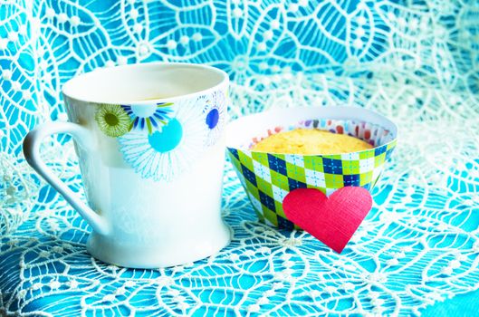 One cupcake on a blue napkin with lace embroidery, a Cup of coffee, a card copy space, the location of cards and holiday invitations.