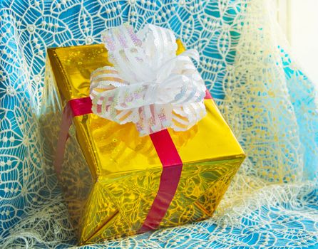 Gift box in gold foil package with white bow, beautiful blue Christmas background, Christmas concept.