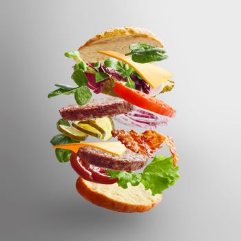 Delicious hamburger with flying ingredients on gray background