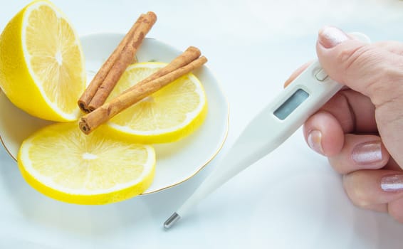 Thermometer in hands, tablets, lemon with cinnamon, the concept of treatment of colds.