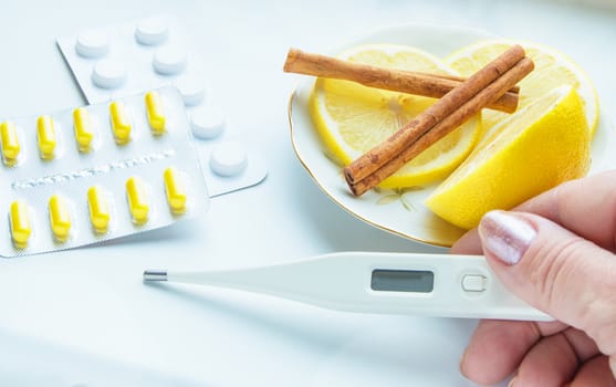 Thermometer in hands, tablets, lemon with cinnamon, the concept of treatment of colds.