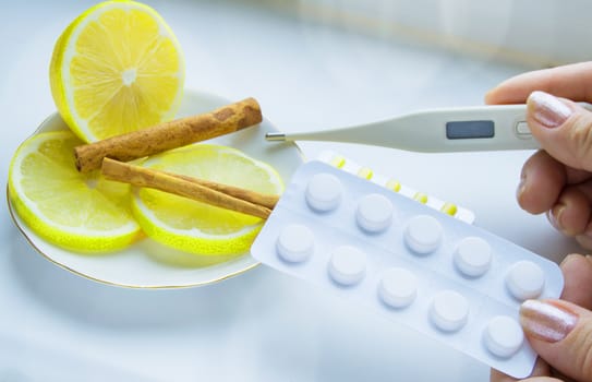 Thermometer in hands, tablets, lemon with cinnamon, the concept of treatment of colds.