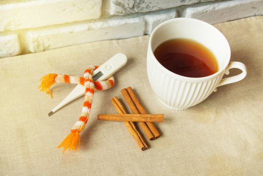 Concept of treating colds - hot tea with cinnamon, thermometer and scarf.