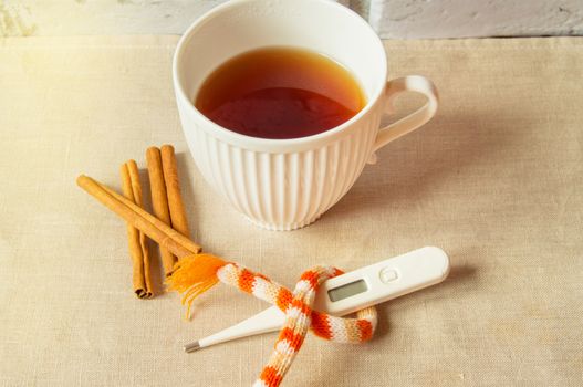 Concept of treating colds - hot tea with cinnamon, thermometer and scarf.